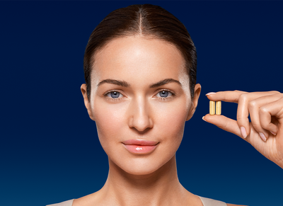 Young woman with smooth skin and hair pulled back holding two BioRewind supplement capsules between her thumb and forefinger